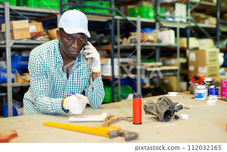 Store warehouse worker takes an order on a mobile phone and makes notes in notebook Store warehouse worker takes an order on a mobile phone and makes notes in notebook 112032165