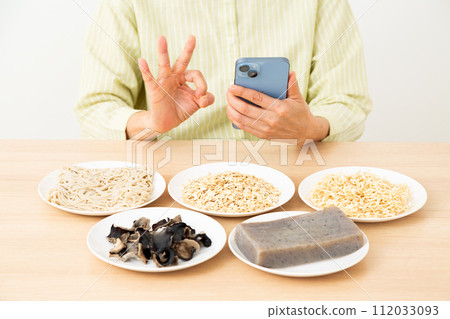 A middle-aged woman holding food containing a lot of dietary fiber and a smartphone and making a circle sign A middle-aged woman holding food containing a lot of dietary fiber and a smartphone and making a circle sign 112033093