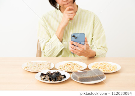 A middle-aged woman worries about food containing a lot of dietary fiber and a smartphone. A middle-aged woman worries about food containing a lot of dietary fiber and a smartphone. 112033094