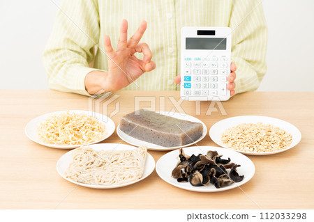 A middle-aged woman makes a circle sign while holding food containing a lot of dietary fiber and a calculator. 112033298