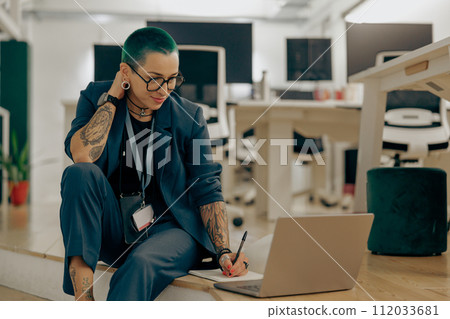 Pretty tattooed business woman with green short hair is use laptop sitting in modern coworking Pretty tattooed business woman with green short hair is use laptop sitting in modern coworking 112033681
