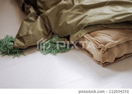 Green and beige blankets lie carelessly on the white floor. Green and beige blankets lie carelessly on the white floor. 112034258