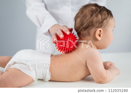 The doctor gently massages the babys neck and muscles with a red ball The doctor gently massages the babys neck and muscles with a red ball 112035280