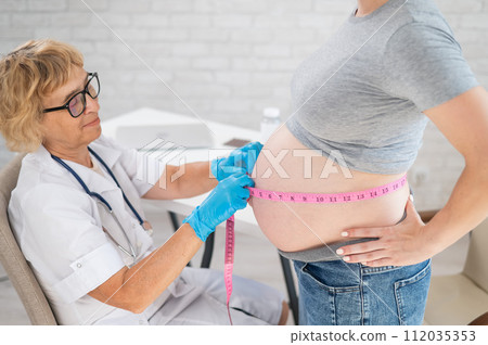 Doctor measuring the volume of a pregnant woman's abdomen using a tape in inches. Doctor measuring the volume of a pregnant woman's abdomen using a tape in inches. 112035353