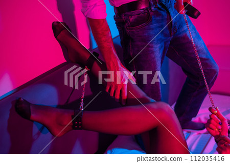 Couple in sexual BDSM games. Woman handcuffed in bed in red hanging neon light.  112035416