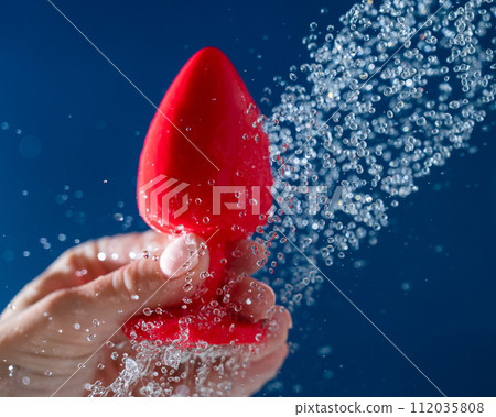 Woman washing red anal plug under shower on blue background. Woman washing red anal plug under shower on blue background. 112035808