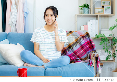 一位年輕女子盤腿坐在客廳打電話給智慧型手機 一位年輕女子盤腿坐在客廳打電話給智慧型手機 112035848