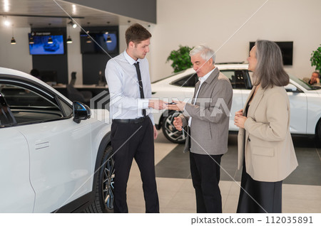 A salesman hands over the keys to a new car to an elderly Caucasian couple. A salesman hands over the keys to a new car to an elderly Caucasian couple. 112035891