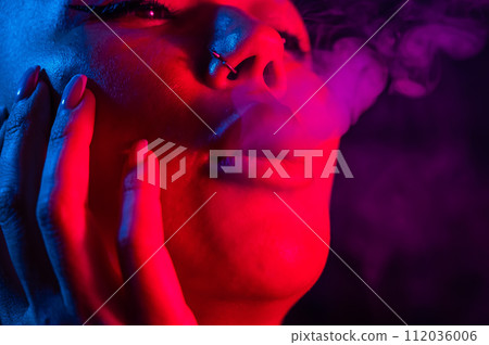 Asian woman with short haircut smoking in neon light. close-up portrait.  112036006