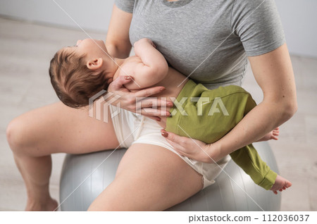 A faceless woman rocks her newborn son on a fitball. A faceless woman rocks her newborn son on a fitball. 112036037