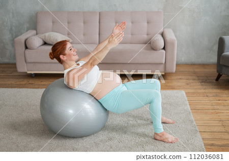 Pregnant red-haired woman doing exercises on fitness ball at home. Pregnant red-haired woman doing exercises on fitness ball at home. 112036081
