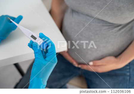 Pregnant woman with fever at doctor's appointment. Therapist holds an electronic thermometer with a temperature of 37.5.  112036106