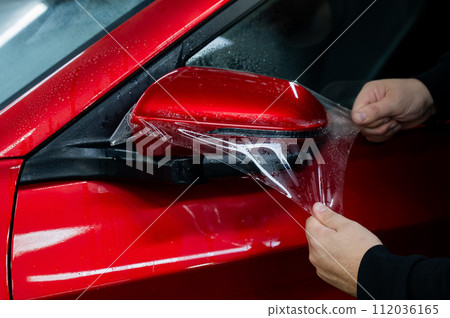 The master applies vinyl film to the side view mirror of a car.  112036165