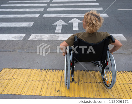 Rear view of an elderly woman on a wheelchair going to a pedestrian crossing.  112036171