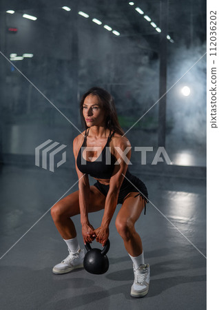 Caucasian woman squats with a kettlebell in the gym. Vertical photo. 112036202