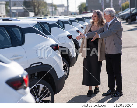 Mature Caucasian couple walks past cars outdoors, choosing a new one.  112036204