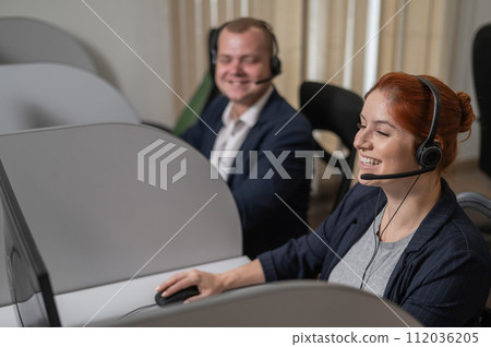 Two friendly call center employees answer customers by phone. Man and woman woman talking on a headset in the office. Two friendly call center employees answer customers by phone. Man and woman woman talking on a headset in the office. 112036205