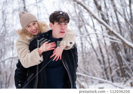 A young couple walks in the park in winter. Guy and girl hugging outdoors. 112036208