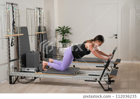 A pregnant woman does a plank on a reformer machine. Perinatal yoga. 112036235