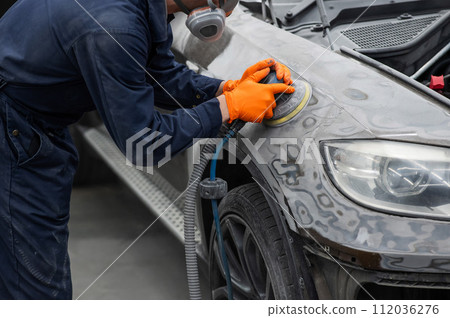 A mechanic sands the putty on a car body with a machine. Repair after an accident. A mechanic sands the putty on a car body with a machine. Repair after an accident. 112036276