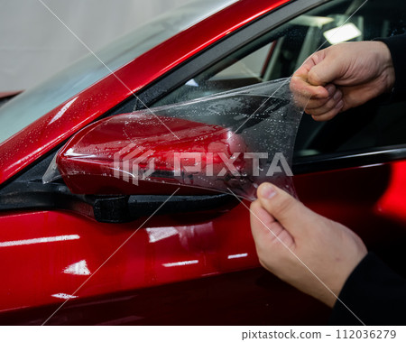 The master applies vinyl film to the side view mirror of a car.  112036279