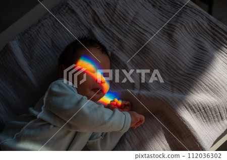 Close-up portrait of a newborn boy with a prism beam on his face. Rainbow. Close-up portrait of a newborn boy with a prism beam on his face. Rainbow. 112036302