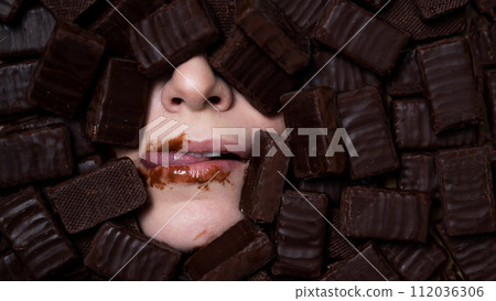 The face of a caucasian woman surrounded by sweets. Girl licks chocolate-stained lips.  112036306