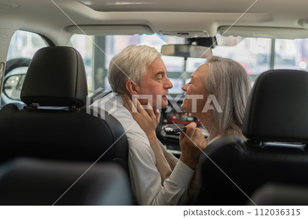Mature Caucasian couple sitting in a new car and rejoicing at the purchase.  112036315