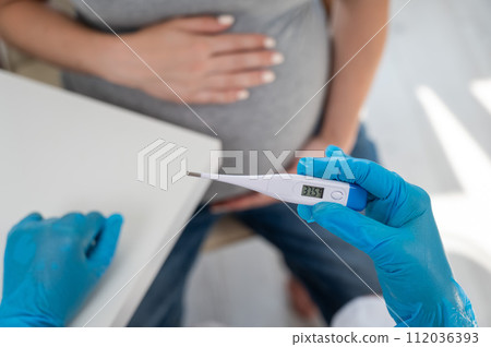 Pregnant woman with fever at doctor's appointment. Therapist holds an electronic thermometer with a temperature of 37.5. Pregnant woman with fever at doctor's appointment. Therapist holds an electronic thermometer with a temperature of 37.5. 112036393