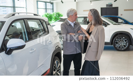 An elderly Caucasian couple chooses a new car at a car dealership. An elderly Caucasian couple chooses a new car at a car dealership. 112036492