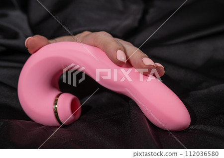 A woman holds a pink curved vibrator while lying on a black silk sheet. A woman holds a pink curved vibrator while lying on a black silk sheet. 112036580
