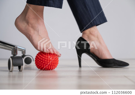 Business woman massages her feet on a massage ball with spikes. 112036600