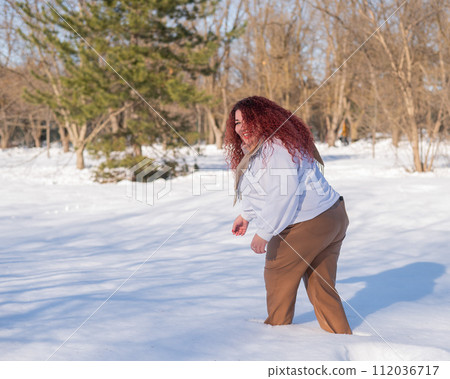 A fat red-haired woman in a white sweatshirt walks through snowdrifts. A fat red-haired woman in a white sweatshirt walks through snowdrifts. 112036717