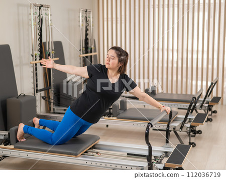 Overweight caucasian woman doing pilates exercises on a reformer. Overweight caucasian woman doing pilates exercises on a reformer. 112036719