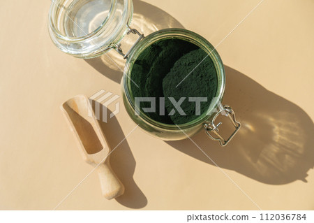 Organic blue-green algae spirulina powder food in glass jar with wooden spoon. Health benefits of spirulina chlorella. Vitamins and minerals to diet. Detox dietary supplement Seaweed superfood 112036784