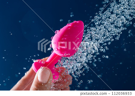 Woman washing pink anal plug under shower on blue background.  112036933
