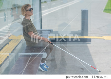 An elderly blind woman is waiting for transport at a bus stop. 112036960