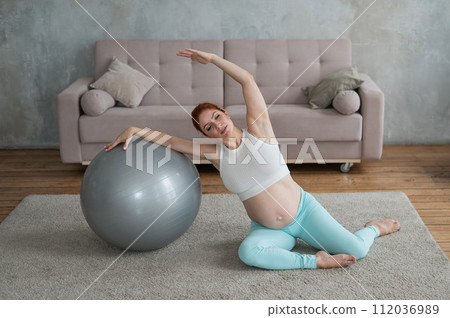 Pregnant woman doing side bends with a fitness ball at home. Pregnant woman doing side bends with a fitness ball at home. 112036989
