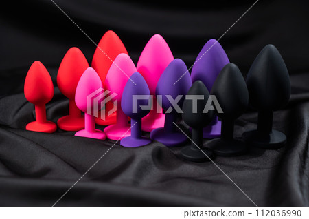 A set of silicone anal plugs in different colors and sizes on a black silk sheet. A set of silicone anal plugs in different colors and sizes on a black silk sheet. 112036990