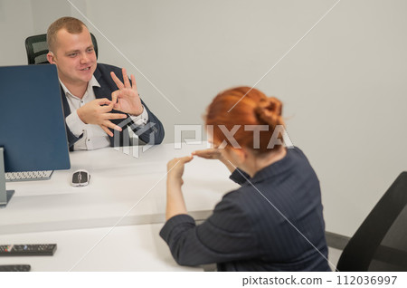 Business partners communicate in sign language. A deaf boss gives a task to a subordinate woman. Business partners communicate in sign language. A deaf boss gives a task to a subordinate woman. 112036997