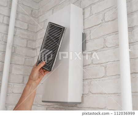 A man changes the filter at the supply ventilation. Gadget for ventilation, disinfection and air purification of the apartment. 112036999