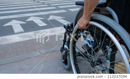 Rear view of an elderly woman in a wheelchair going to a pedestrian crossing. Close-up on wheels. Rear view of an elderly woman in a wheelchair going to a pedestrian crossing. Close-up on wheels. 112037094