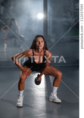 A beautiful brunette with big breasts does Russian swings with a kettlebell. Vertical photo. A beautiful brunette with big breasts does Russian swings with a kettlebell. Vertical photo. 112037095