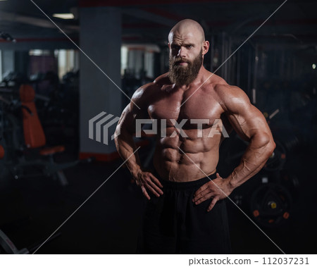 Muscular bald man posing shirtless. Bodybuilder showing off his shape in the gym. Muscular bald man posing shirtless. Bodybuilder showing off his shape in the gym. 112037231