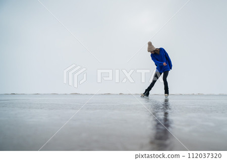 Caucasian woman in a blue sweater is skating on a frozen lake. The figure skater performs the program. 112037320