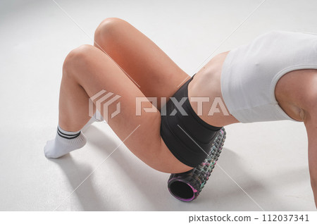 Faceless woman doing roller exercise for myofascial release on white background. Self-massage of thighs.  112037341
