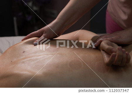 Woman having a therapeutic back massage. The masseur kneads the muscles under the shoulder blade. Woman having a therapeutic back massage. The masseur kneads the muscles under the shoulder blade. 112037347