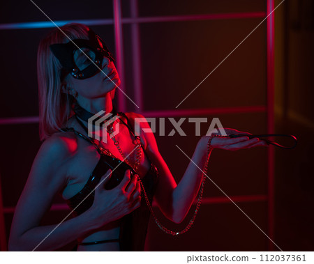 Blonde girl in a leather mask and handcuffs in the bedroom in red blue neon light. Role-playing games. Blonde girl in a leather mask and handcuffs in the bedroom in red blue neon light. Role-playing games. 112037361
