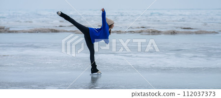 Caucasian woman in a blue sweater is skating on a frozen lake. Figure skater performs a swallow.  112037373