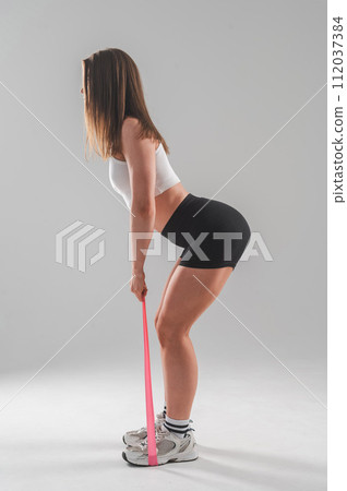 Caucasian woman doing exercises with fitness elastic band on white background. Vertical photo. Caucasian woman doing exercises with fitness elastic band on white background. Vertical photo. 112037384